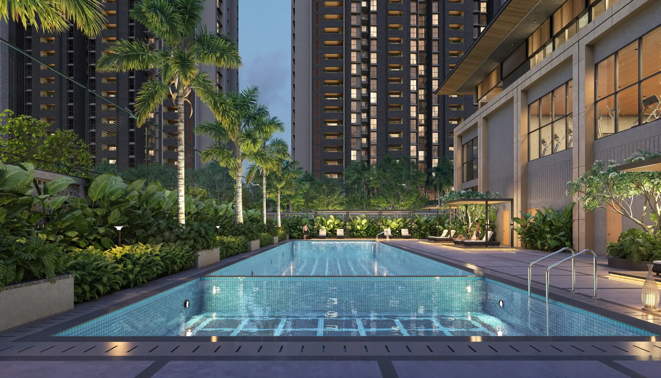 The clubhouse at dusk beside a lit swimming pool, palms and planting all around.