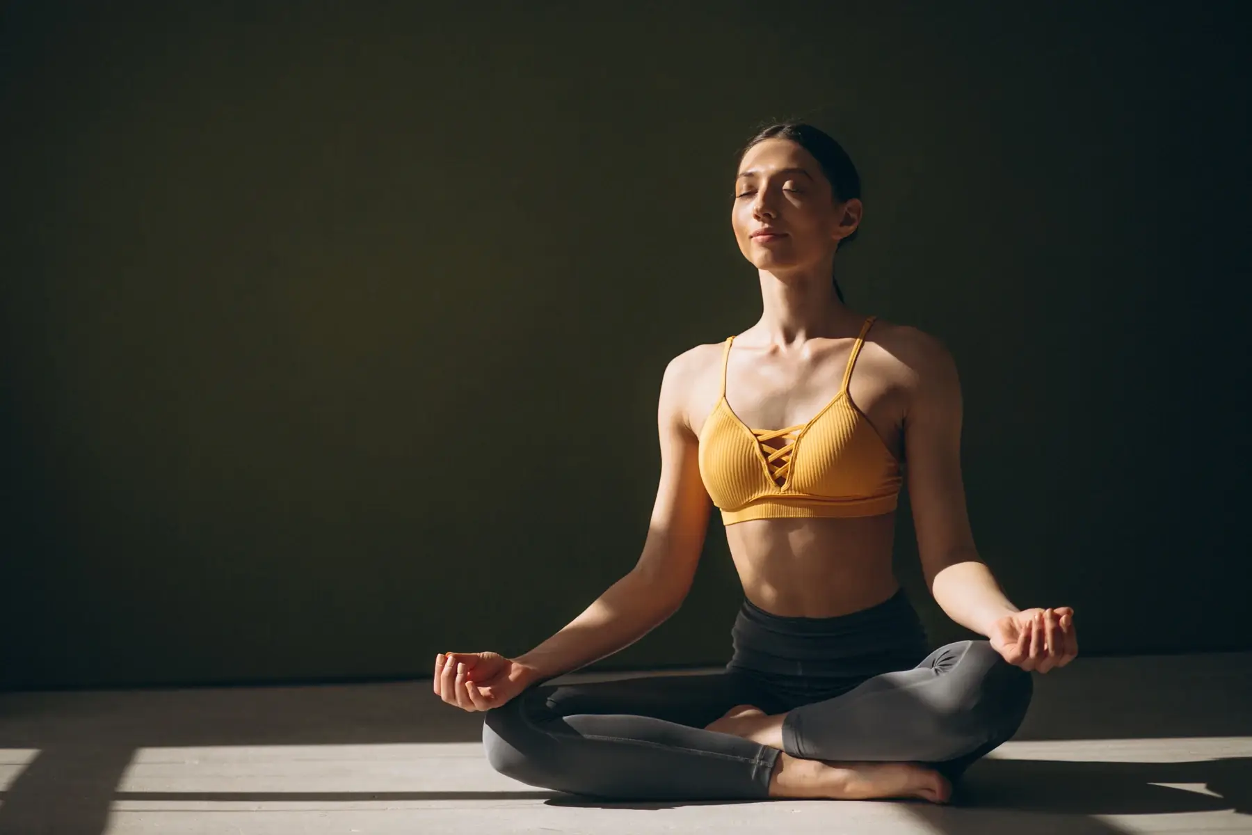 A woman meditating cross-legged in warm light in the yoga room.